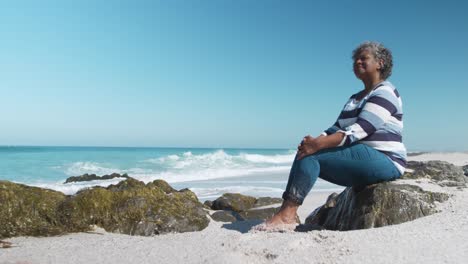 ältere frau sitzt auf einem felsen am strand