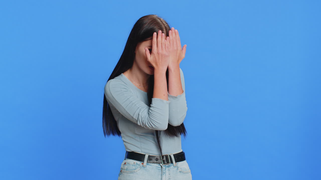 Curiosa giovane donna caucasica che si copre gli occhi con la mano e spia tra le dita, nascondendosi e sbirciando