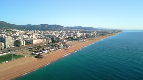 scenic panoramic view of calella de mar coastal town in maresme, barcelona. sandy beach stretches along turquoise mediterranean sea with mountains in background