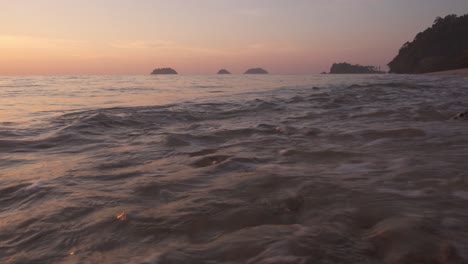 beach with sand and small rocks with islands and headland in distance shot at sunset