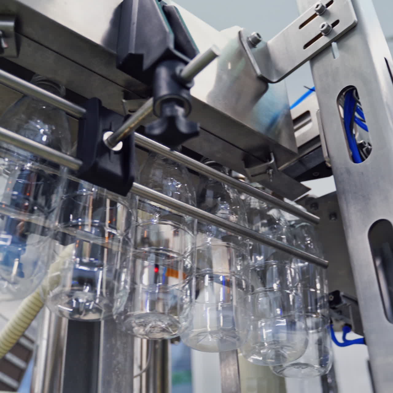 Empty plastic bottles hanging from a conveyor line. Bottle production line. View from below on plastic bottles for liquid in modern milk plant.