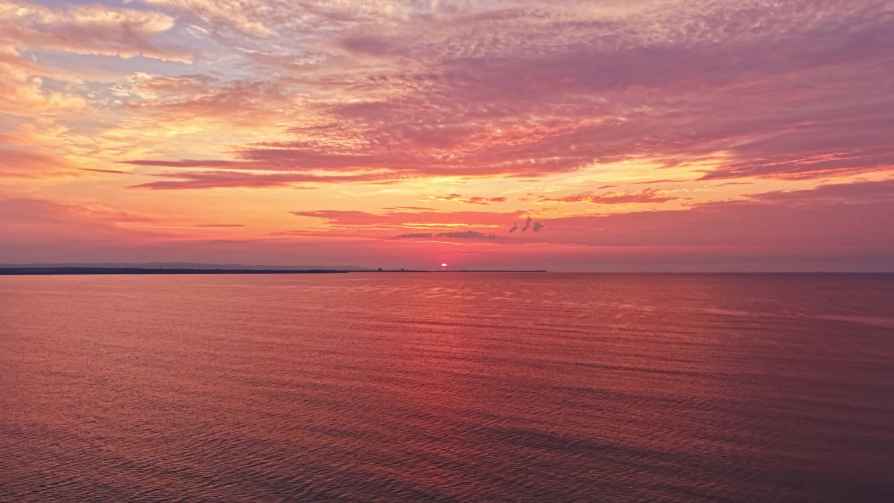 Farverig solnedgang over det rolige hav med skyer, der reflekterer sollys om aftenen