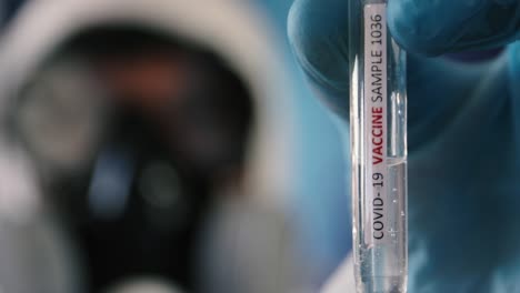 scientist holds up test tube with coronavirus vaccine while wearing protective equipment