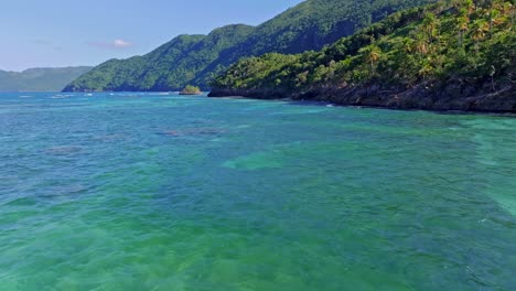 Drone-flight-over-green-and-blue-clear-Caribbean-sea-water-along-green-coastline-in-summer