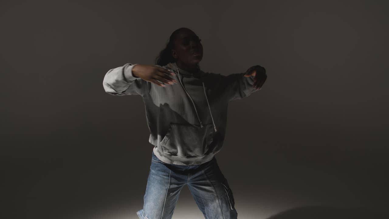 retrato de estudio de una mujer joven con capucha bailando con iluminación baja contra un fondo gris 10