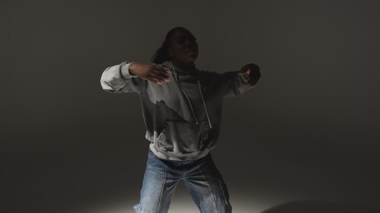 Studio Portrait Shot Of Young Woman Wearing Hoodie Dancing With Low Key Lighting Against Grey Background 10