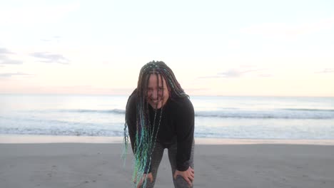 mujer con trenzas sonríe cansada después de correr en la playa