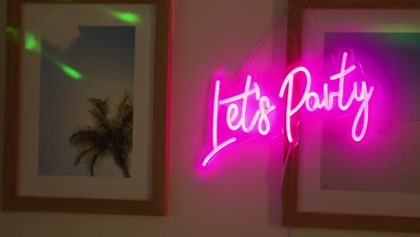 close up of neon let's party sign hanging on wall at house party