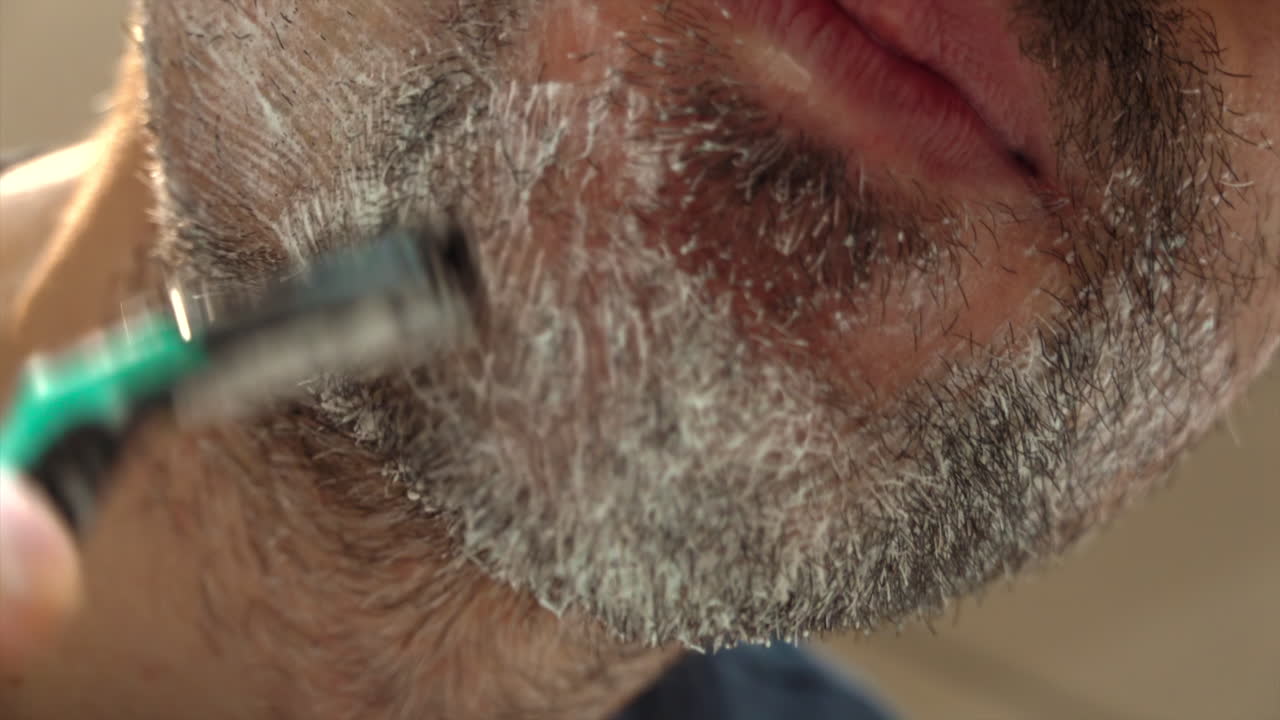 Close up of a man shaving his beard with a green and black razor