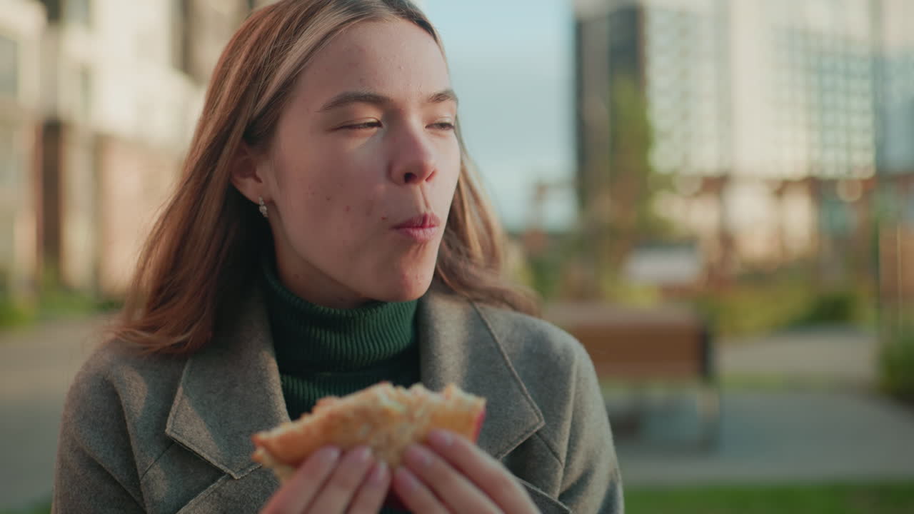 Close up young lady outdoors holding pizza slice making toast gesture with someone out of frame, soft daylight highlighting casual moment with relaxed expression