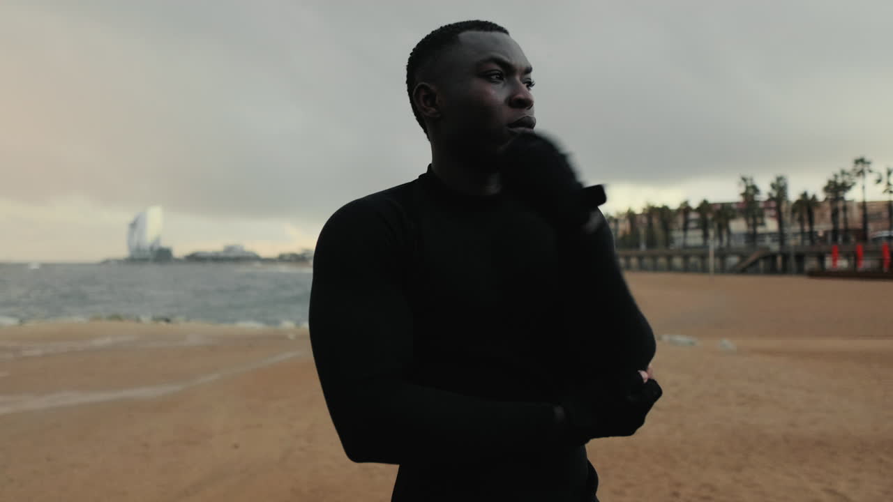 Nuori tummaihoinen mies venyttelee käsiään rannalla ennen treeniä