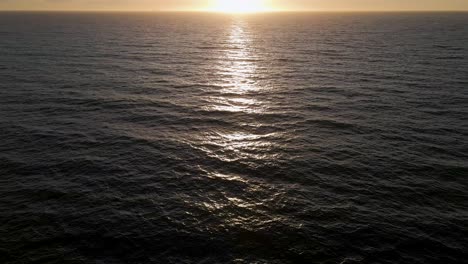 sunset over pacific ocean, aerial tilt-up reveal of sun setting over sea horizon