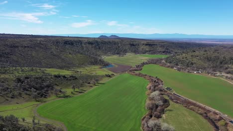 Sobrevuelo-De-Drones-De-600&#39;-Sobre-Un-Valle-Verde-Bordeado-De-Montañas-Y-Un-Arroyo-Bordeado-De-árboles-Que-Atraviesa-El-Centro