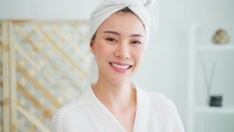 Portrait-of-Asian-client-woman-looking-at-camera-after-doing-therapy.-Attractive-girl-feeling-happy-and-relax,-sit-on-massage-table-after-doing-physiotherapy-for-skin-and-body-care-in-spa-beauty-salon