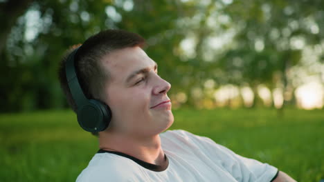 close up of young boy wearing headphones nodding head while enjoying music with a subtle smile, looking up, tattooed hand visible, background features vibrant trees and lush greenery