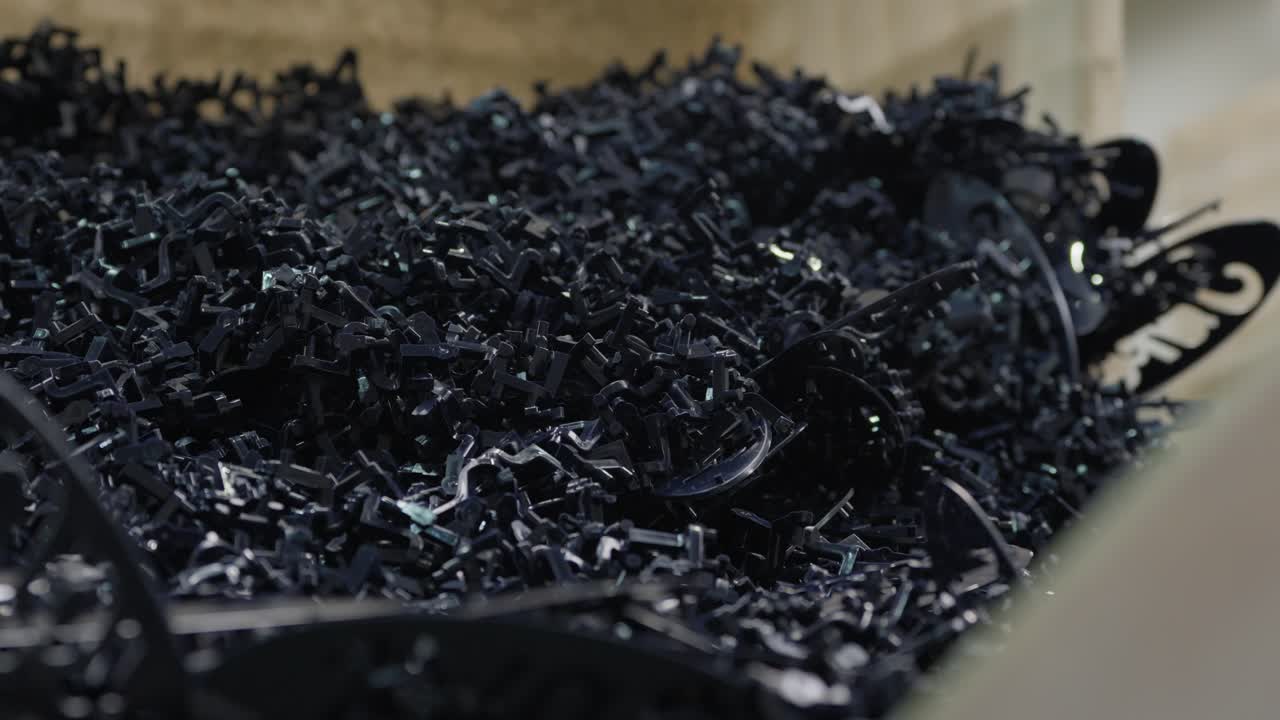 Heap of shredded black rigid plastic fragments and curled strips piled in recycling facility