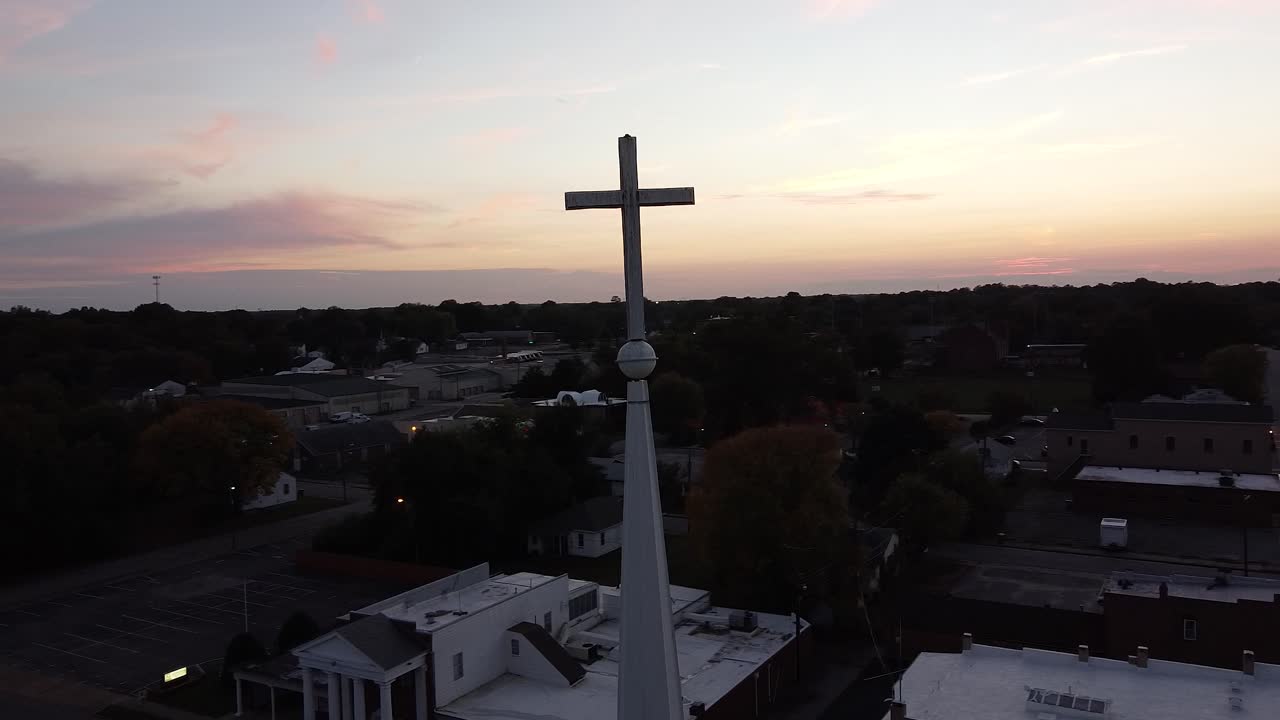 drone en órbita alrededor de la cruz en un campanario de la iglesia con una hermosa puesta de sol sobre el horizonte de la ciudad