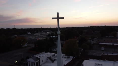 drone orbit around cross on a church steeple with a gorgeous sunset over the city skyline