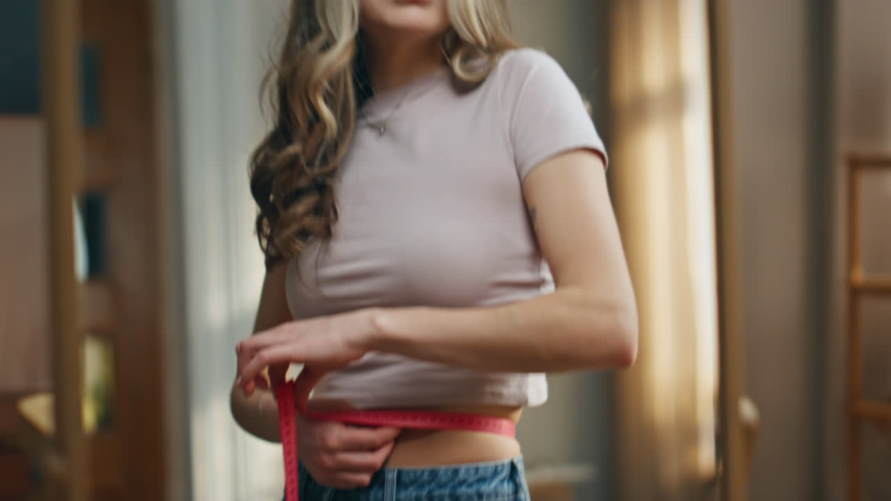 Woman measuring her waist with measuring tape indoors