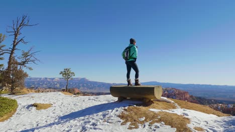 girl woman standing on bench overlooking red rocks formation and snow near bryce canyon in southern utah