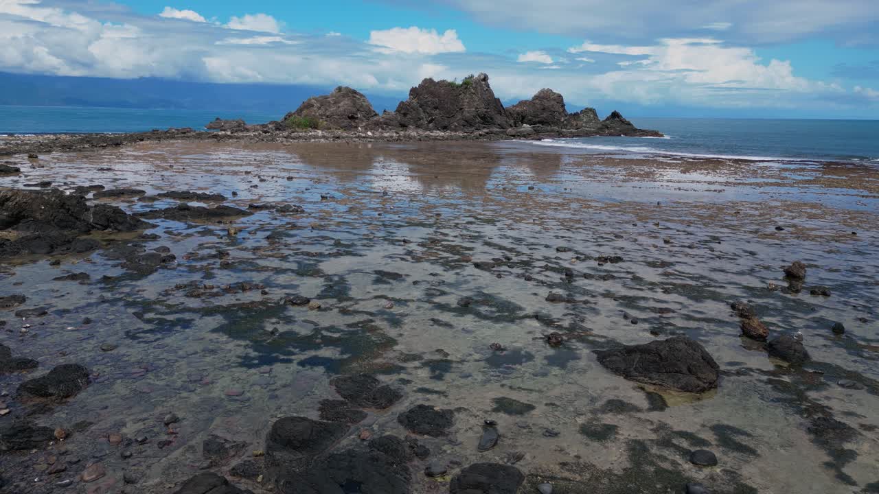 A captivating drone shot captures the small rock mountains scattered along the shore, standing tall against the magnificent backdrop of the ocean.