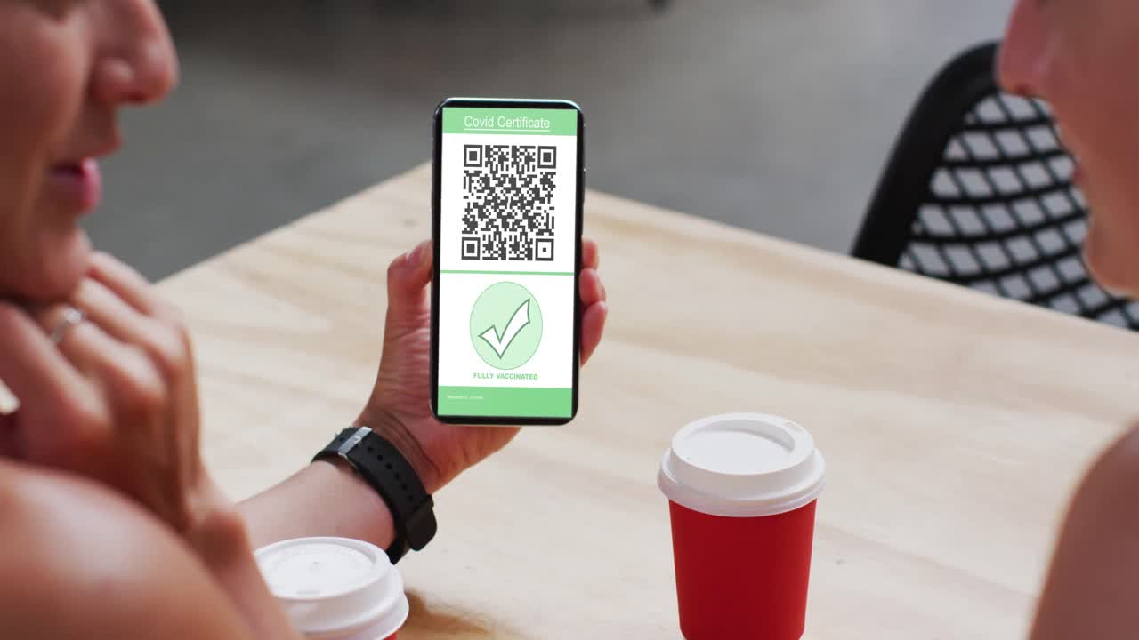 Man at cafe showing smartphone with covid vaccination certificate and qr code on screen