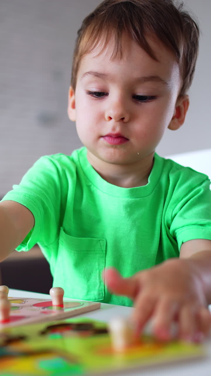 Un adorabile bambino che tiene in aria un pezzo di puzzle. Il bambino guarda attentamente dove mettere il puzzle. Video verticale