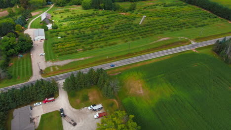 Aerial Tracking Shot of Blue Car Traveling Down Rural Farmland with Homes Wisconsin