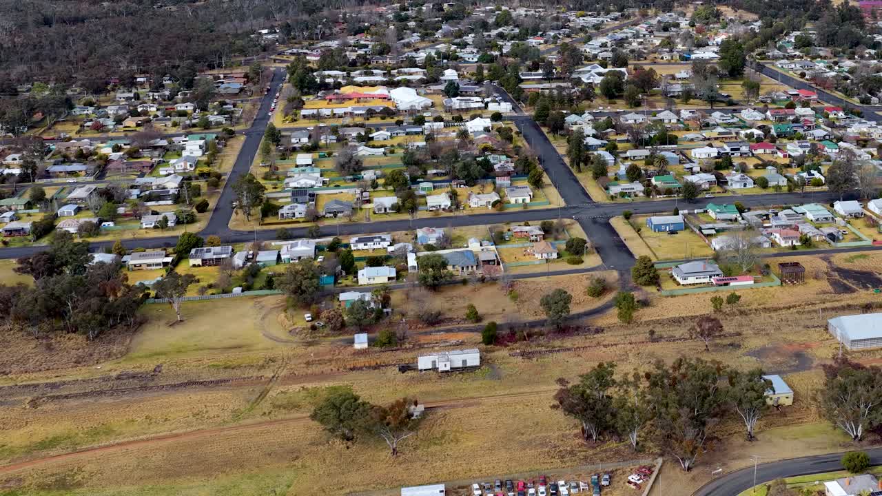 Drone footage glides over suburban Coonabarabran, New South Wales, revealing houses, roads, and greenery under overcast daylight with smooth, steady camera movement