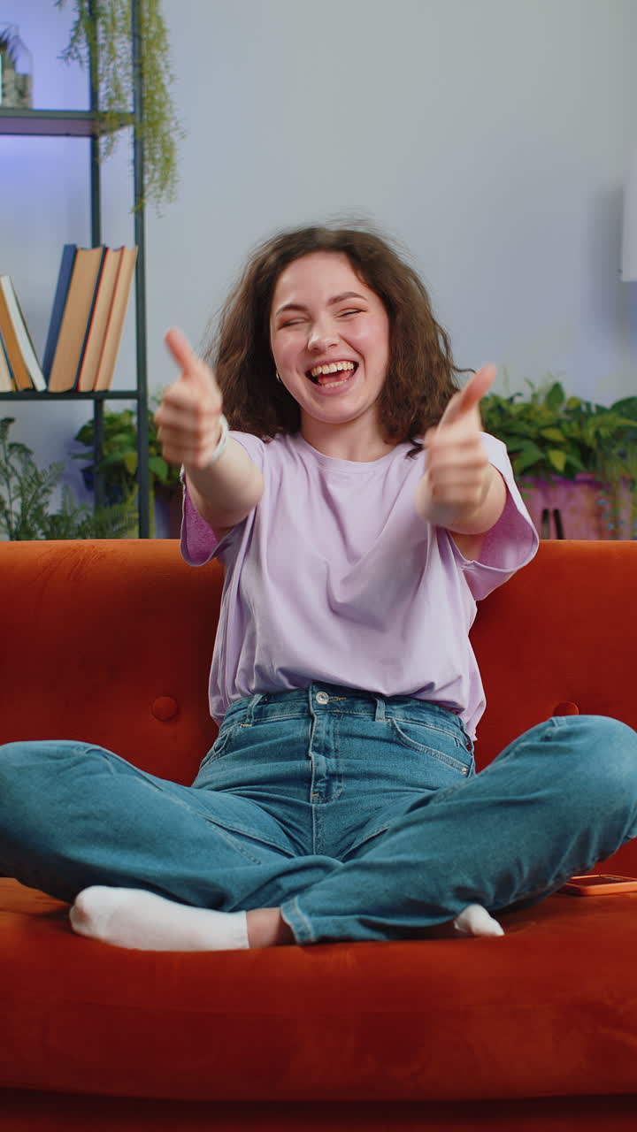 Happy young woman looking approvingly at camera showing thumbs up like positive sign good news