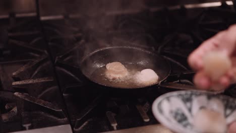cook puts the chicken in a frying pan with hot oil in a restaurant kitchen with his hands