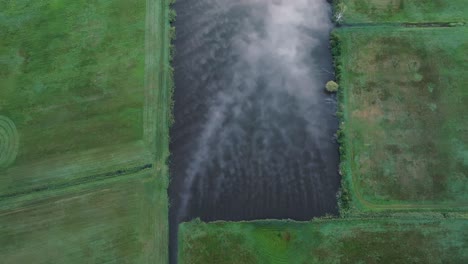 Misty River Flowing Through Green Fields - Aerial View