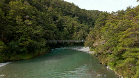 Turistas-Cruzando-El-Puente-De-Metal-Sobre-El-Río-Verde-Rápido-En-La-Pista-De-Las-Piscinas-Azules-En-Nueva-Zelanda