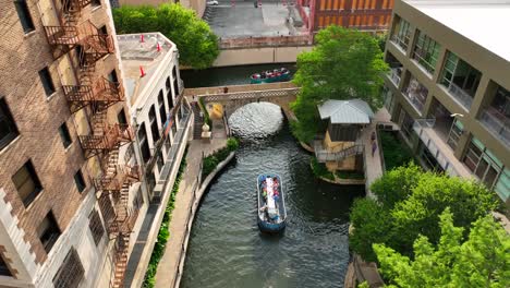 Boat-and-barge-passes-under-bridge-beside-San-Antonio-River-Walk-Park