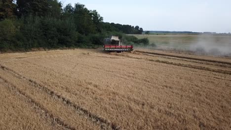 A-cinematic-4K-drone-shot-of-a-combine-harvester-harvesting-a-field-in-France,-showcasing-agriculture-with-an-epic-view-and-dramatic-dust