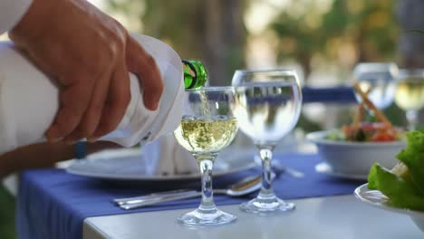 the waiter pours white wine in wine glass in the restaurant