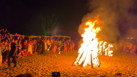 Exotic fire dancers performing at traditional bonfire summer festival at the beach at the San Juan celebration in Marbella Spain, enjoying a fun party, big burning fire, hot flames at night, 4K shot