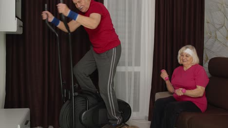 senior mature grandfather and grandmother using orbitrek, doing weight lifting dumbbells exercises