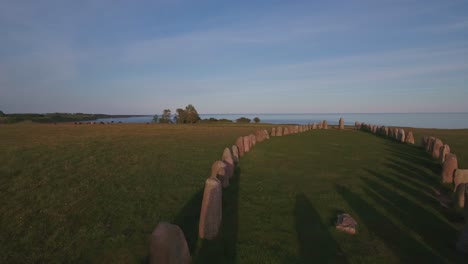 Ancient-Oval-Formed-Rocks-Ales-Stenar-By-The-Summer-Evening-In-South-Sweden-Skåne-Österlen-Kåseberga,-Aerial-Low-Smooth-Forward