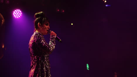 a woman in a sparkly dress singing on stage at a concert