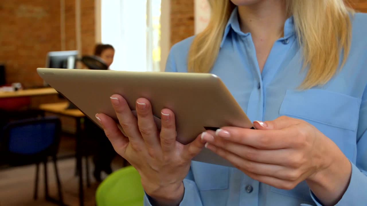 una mujer joven y atractiva usando una tableta negra con pantalla verde en una oficina moderna.