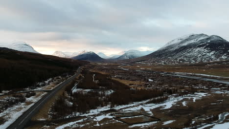 Aerial-View-of-Icelandic-Highlands,-Road,-Snow-in-a-Field-and-Mountain-Peaks-on-Cloudy-Day,-Drone-Shot