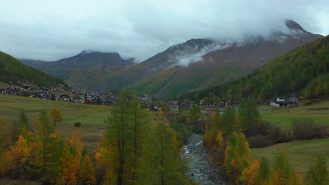 Fall-autumn-larch-forest-trees-aerial-drone-village-Saas-Fee-Swizerland-gray-grey-rainy-fog-mist-moody-Swiss-Alps-mountain-peaks-Feevispa-River-glacier-glacial-peaceful-valley-cloud-layer-upward