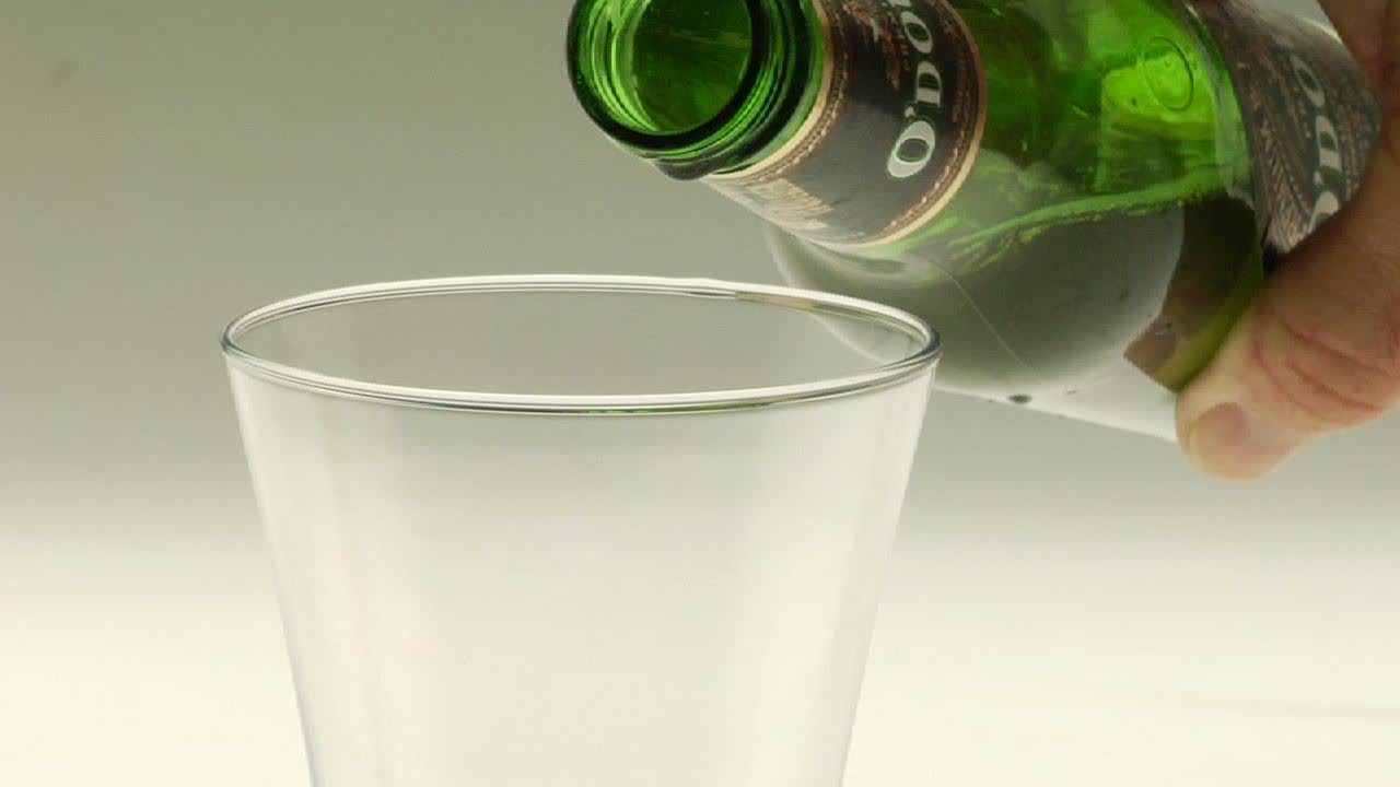 Beer is poured into a Pilsner glass and its foamy head drips over the edge