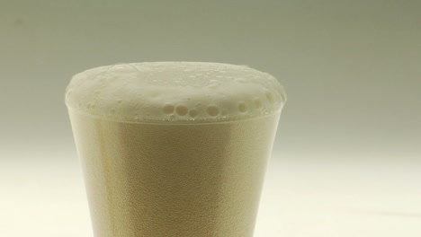 beer is poured into a pilsner glass and its foamy head drips over the edge