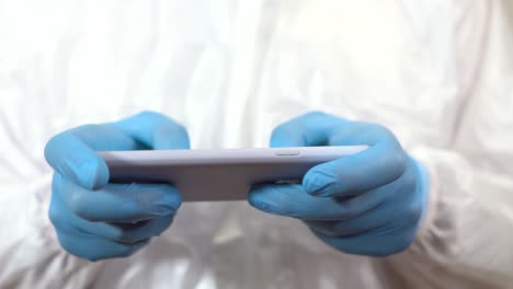 hands of doctor dressed in ppe suit typing and using mobile phone horizontally
