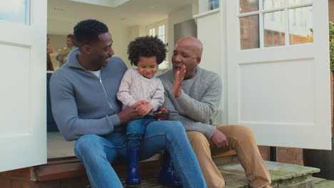 Multi-Generation-Male-Family-Sitting-On-Step-At-Home-Playing-And-Having-Fun-Together