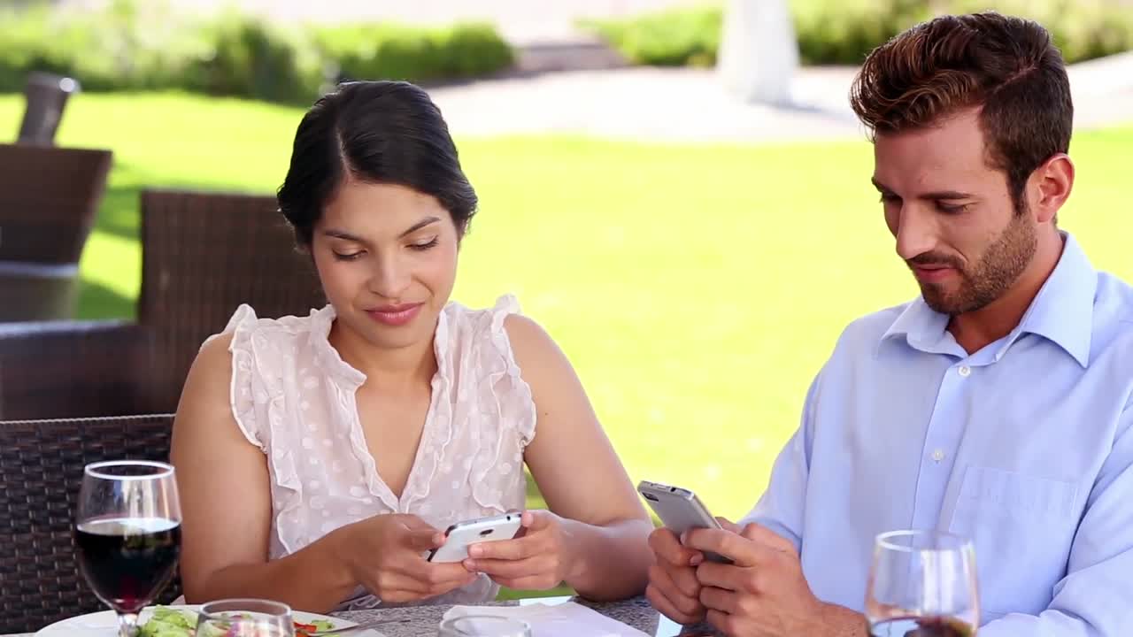 Pareja enviando mensajes de texto en sus teléfonos durante el almuerzo