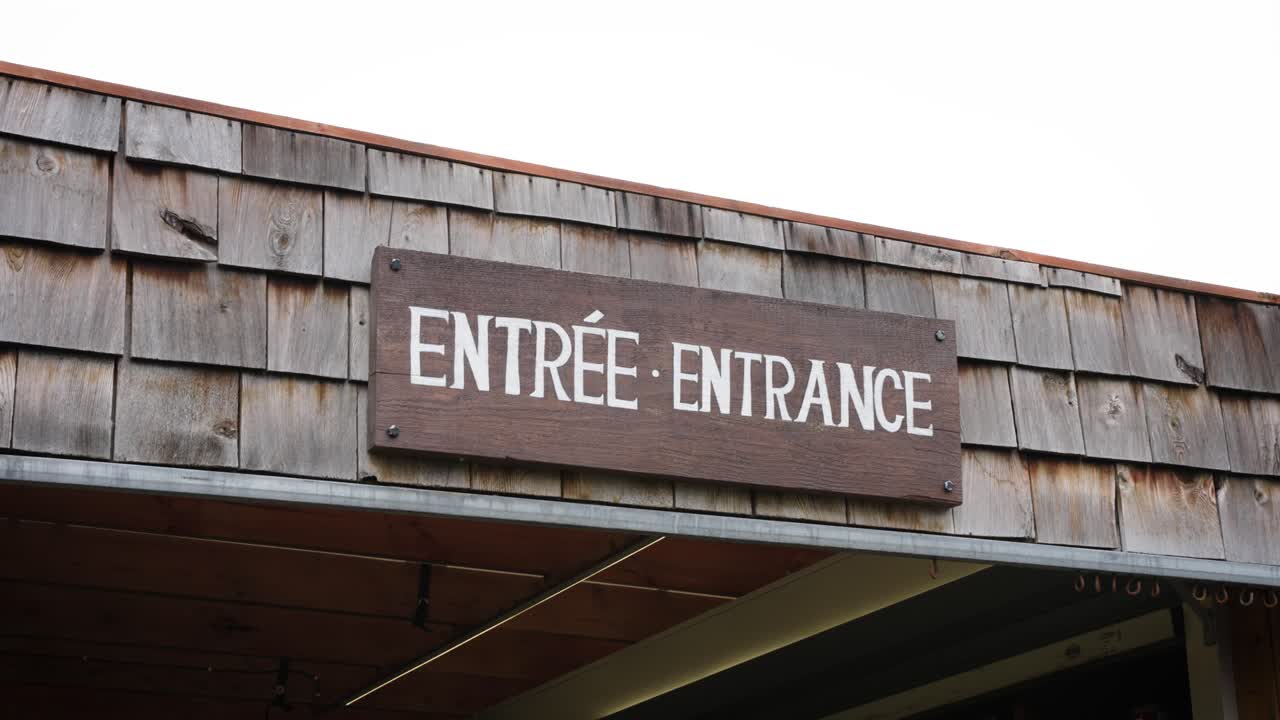 A Rustic Wooden White Painted Entrance Entr&eacute;e Sign Against a Shingled Roof on a Local Canadian Outdoor Farmers Market Business