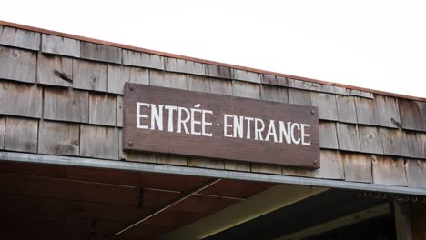 A-Rustic-Wooden-White-Painted-Entrance-Entrée-Sign-Against-a-Shingled-Roof-on-a-Local-Canadian-Outdoor-Farmers-Market-Business